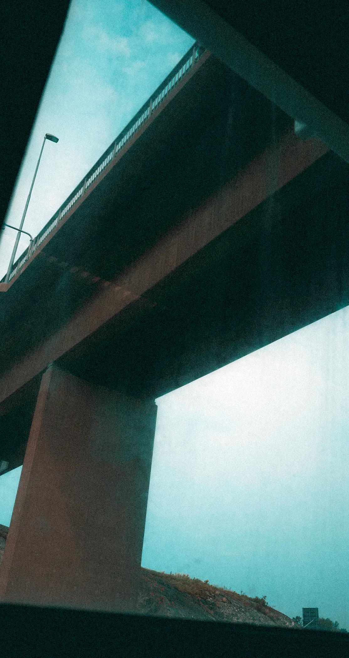 The underside of a concrete overpass against a pale sky