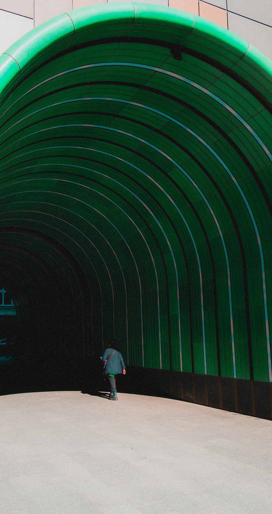 A man walking into a ribbed green tunnel entrance, London