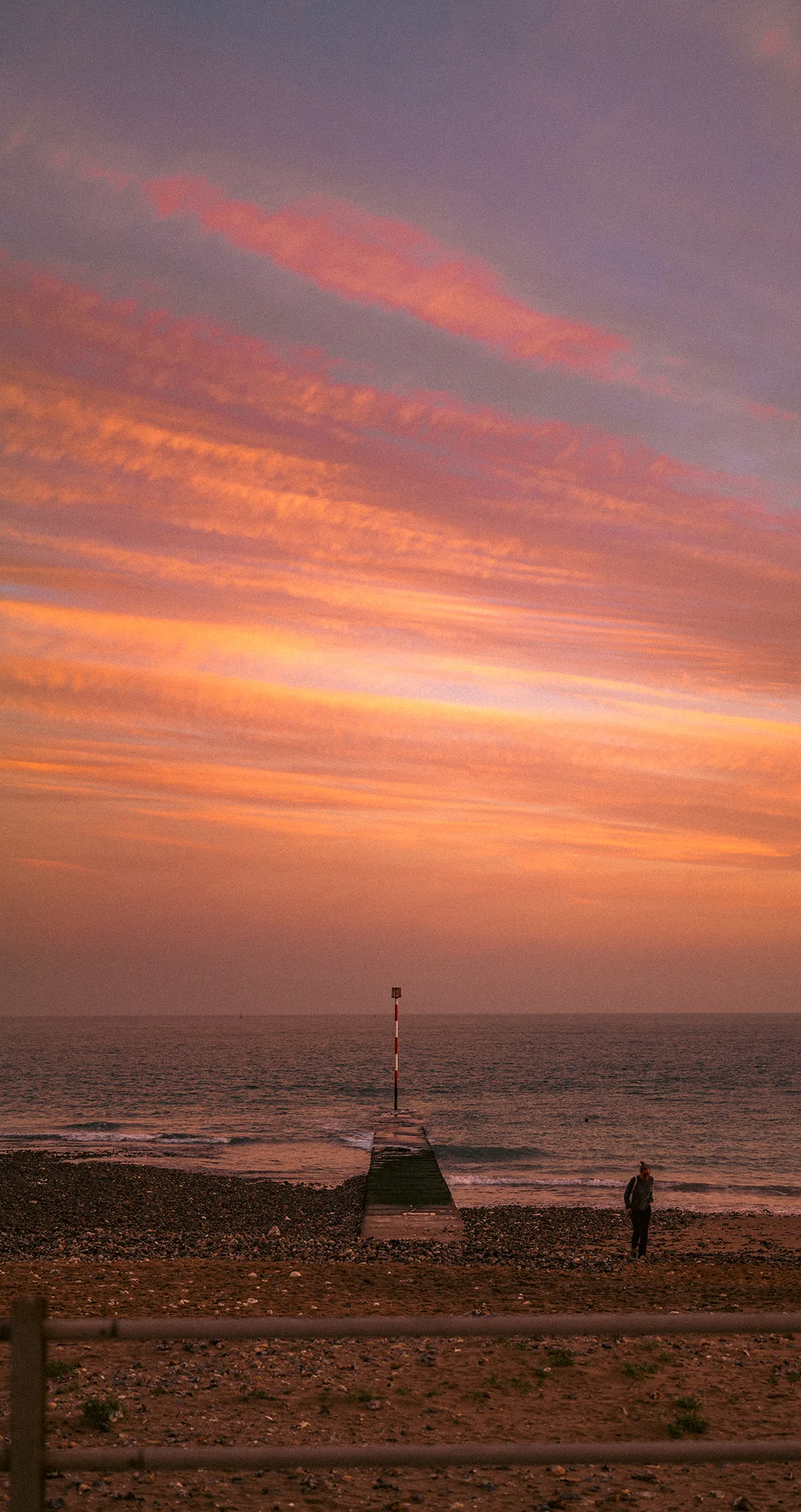 Pink and orange cloud streaks over the beach and a tide marker at dusk, Margate