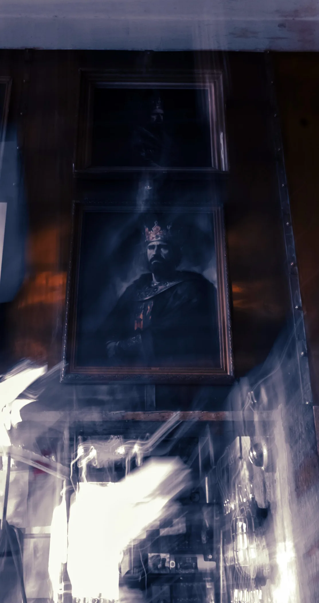 A portrait of a crowned king on a pub wall, blurred by reflections