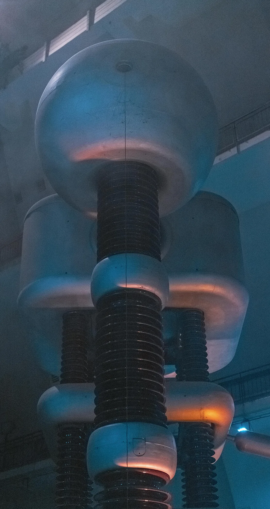 Stacked insulators and polished domes of a high-voltage generator lit in blue and orange