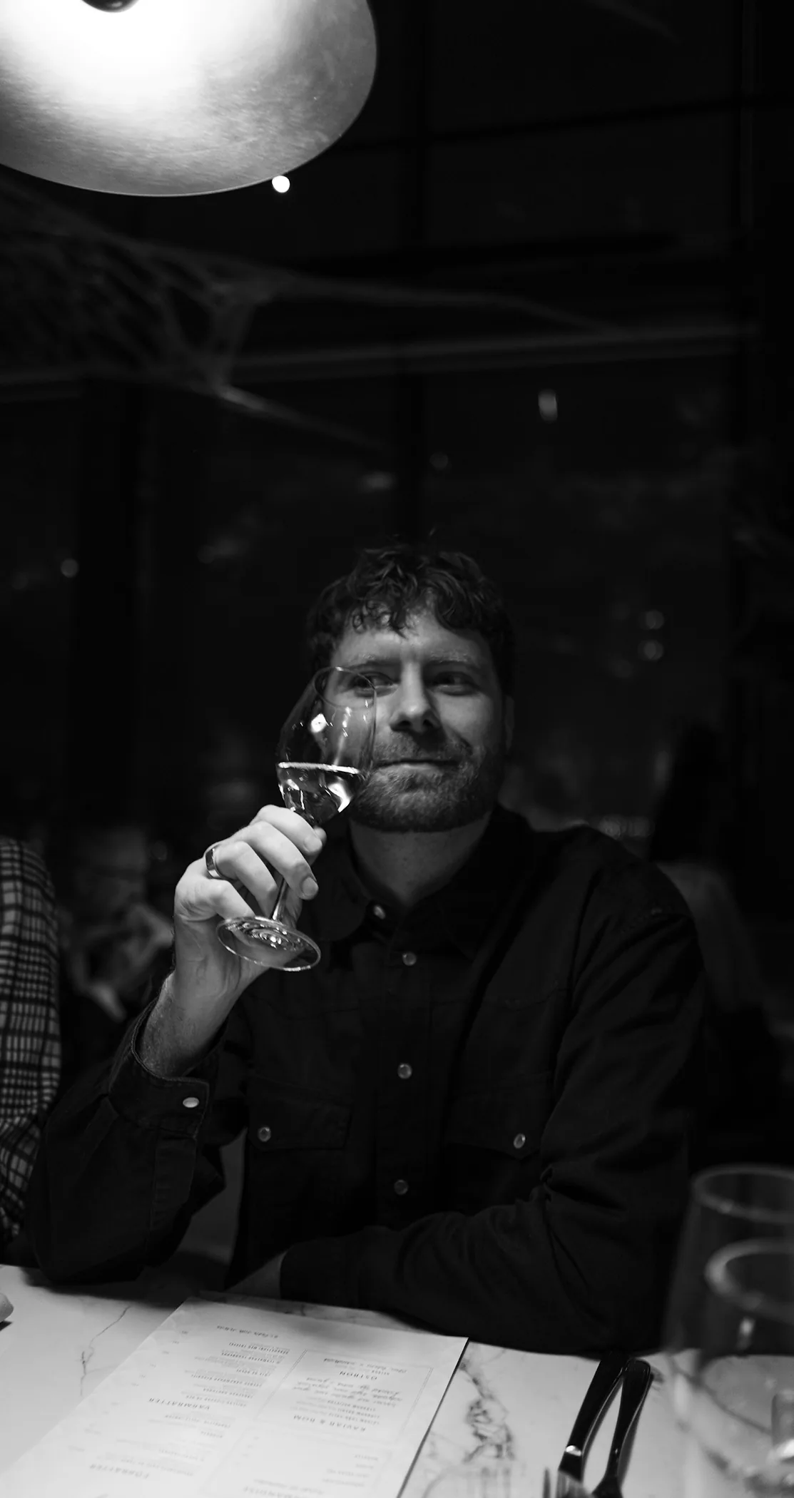 A man raising a glass of wine at a dinner table, in black and white