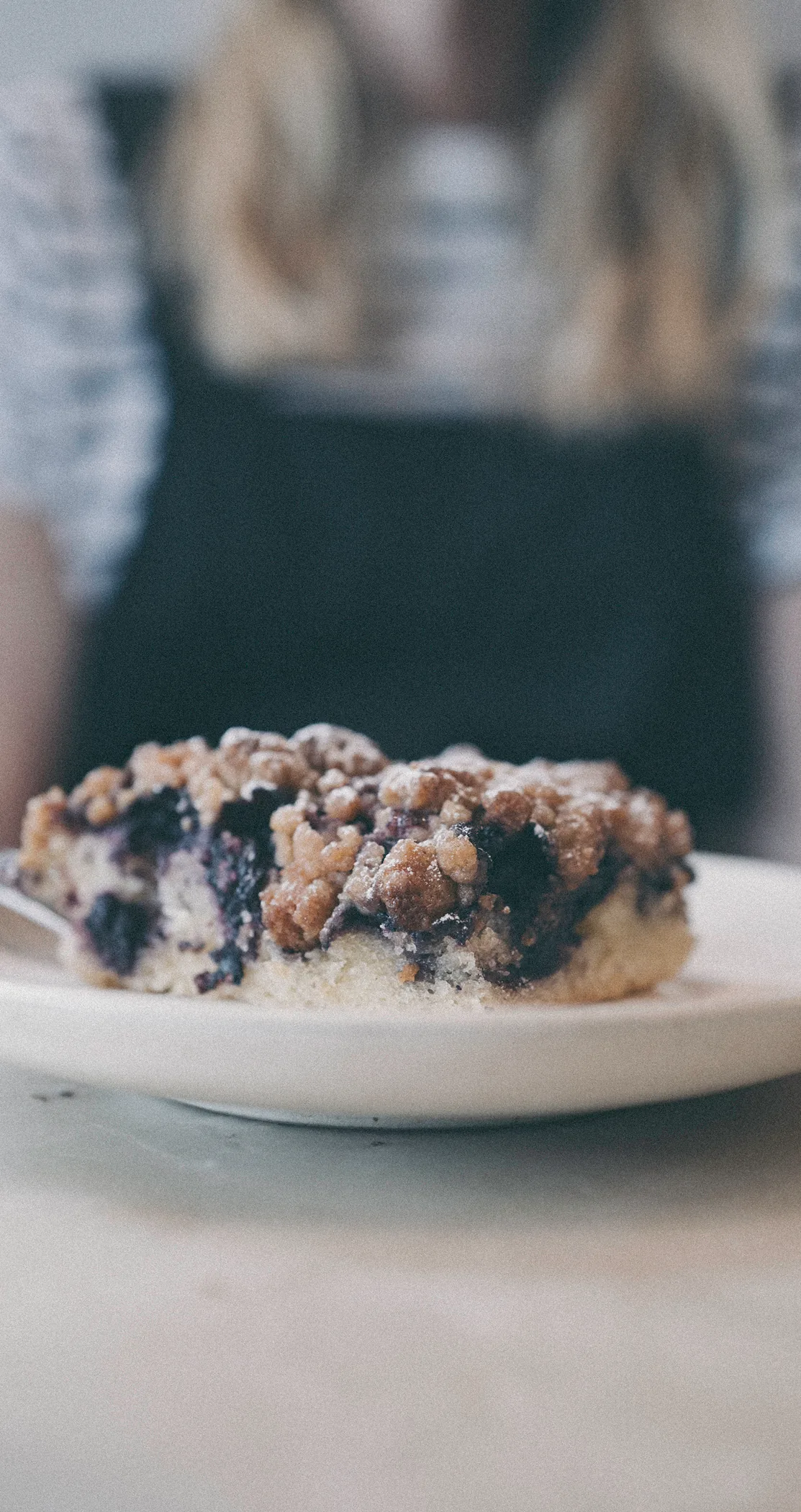 A slice of blueberry crumble on a plate in the foreground