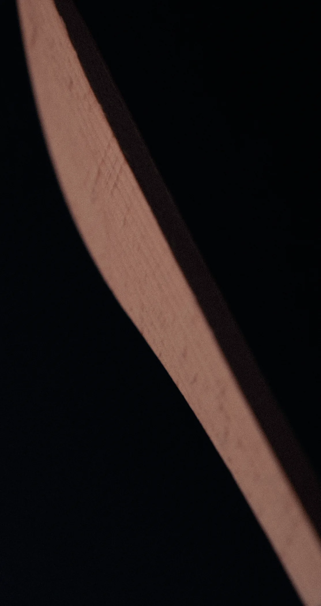 The edge of a wooden blade cutting across darkness